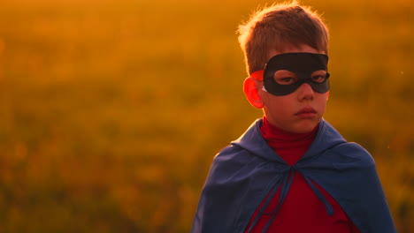 The-boy-in-the-mask-and-Cape-of-a-super-hero-at-sunset-in-a-field.